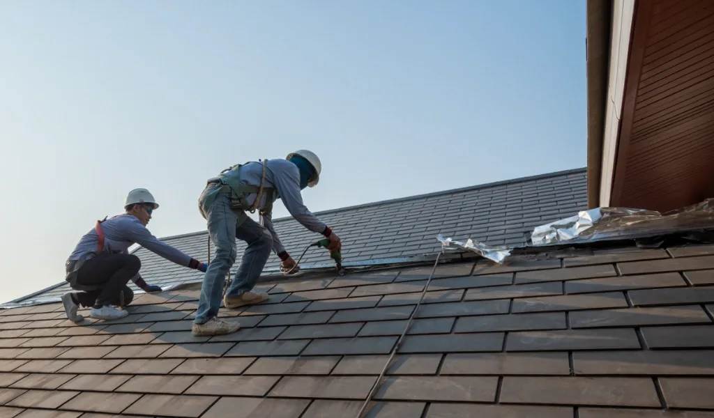 Two roofers installing dark slate tiles on a steep roof
