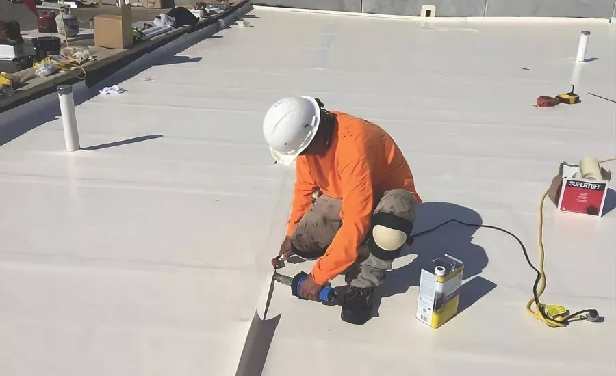 A worker sealing a seam on a white low-slope commercial membrane roof