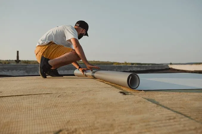 A worker unrolling membrane across a flat commercial roof at sunset