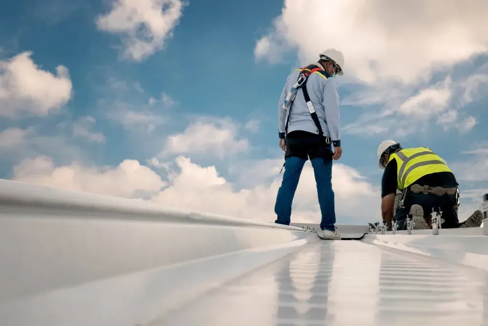 Two roofers working on a white low-slope commercial roof under a cloudy sky