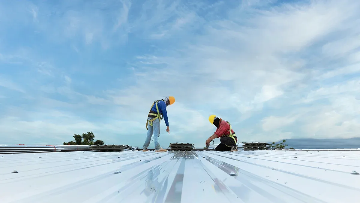 Two roofers on a white metal roof under a bright blue sky