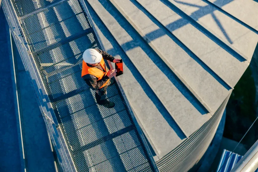 An overhead view of a roofer with a tablet on a metal roof walkway
