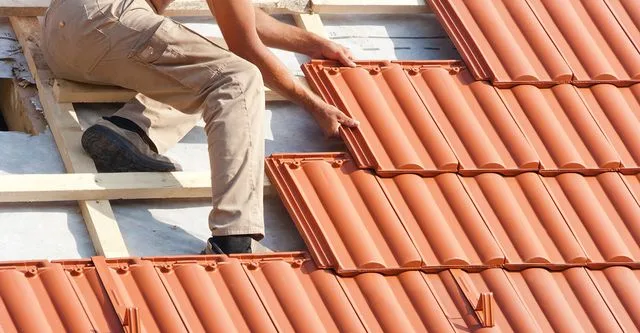 A roofer placing red clay tiles on wood battens