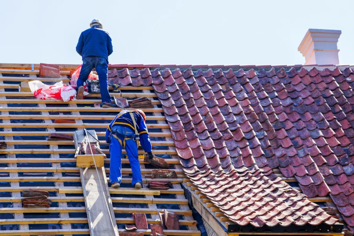Two roofers replacing tiles on a clay-tile roof