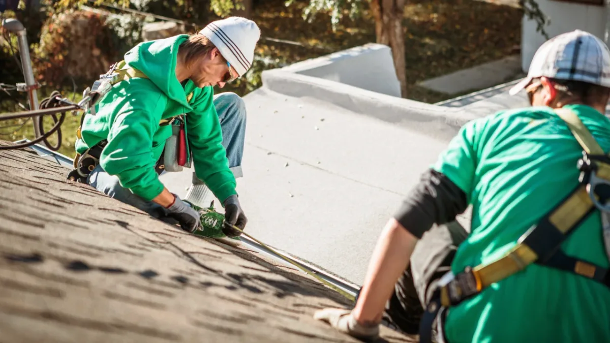 Two roofers measuring on a shingle roof in autumn