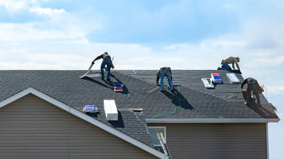 A crew laying underlayment and shingles across a large residential roof