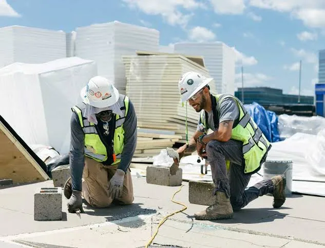 Two roofers working on a flat roof beside stacks of insulation board