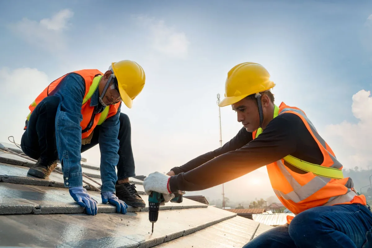 Two roofers drilling grey tile on a roof at sunset
