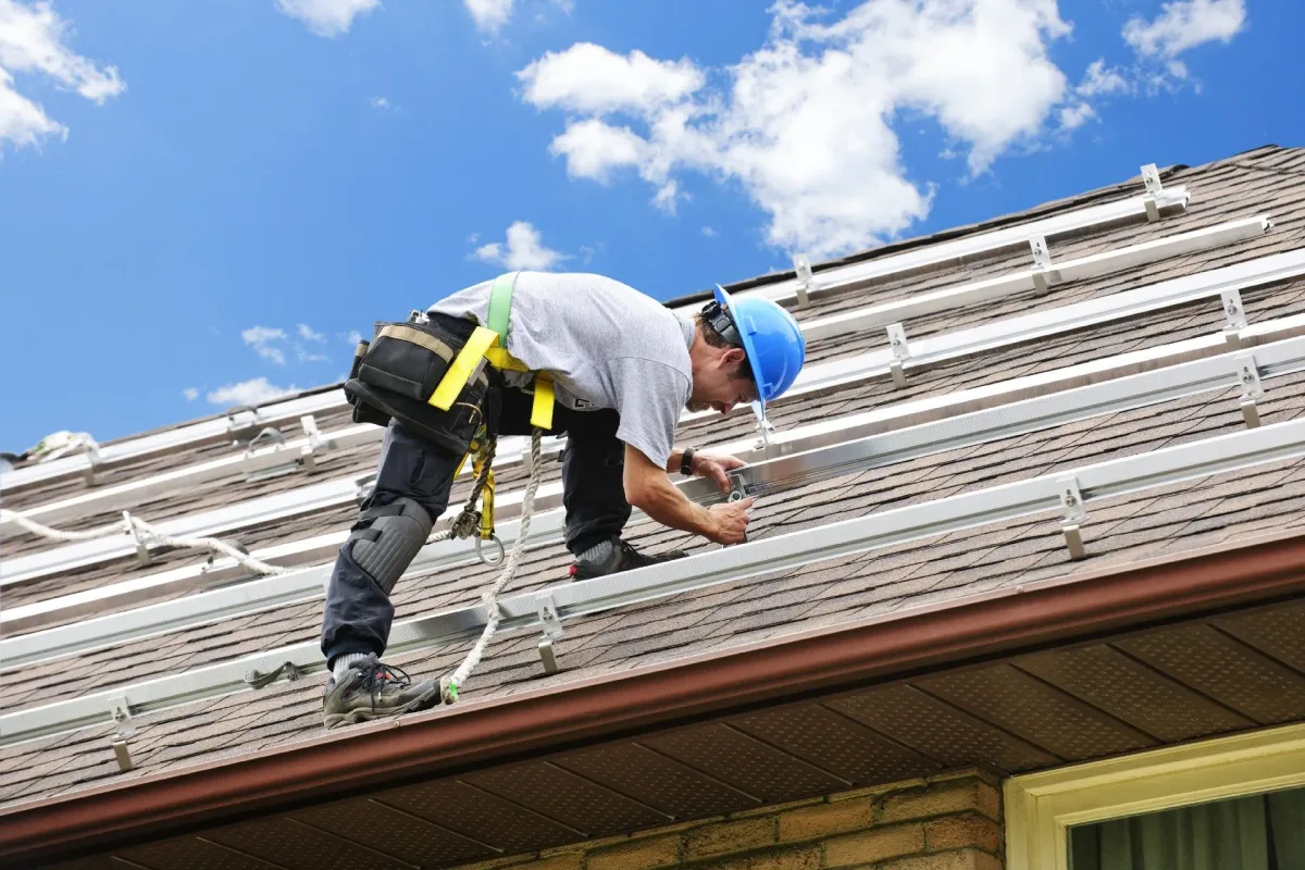 A roofer fastening a blue standing-seam metal roof